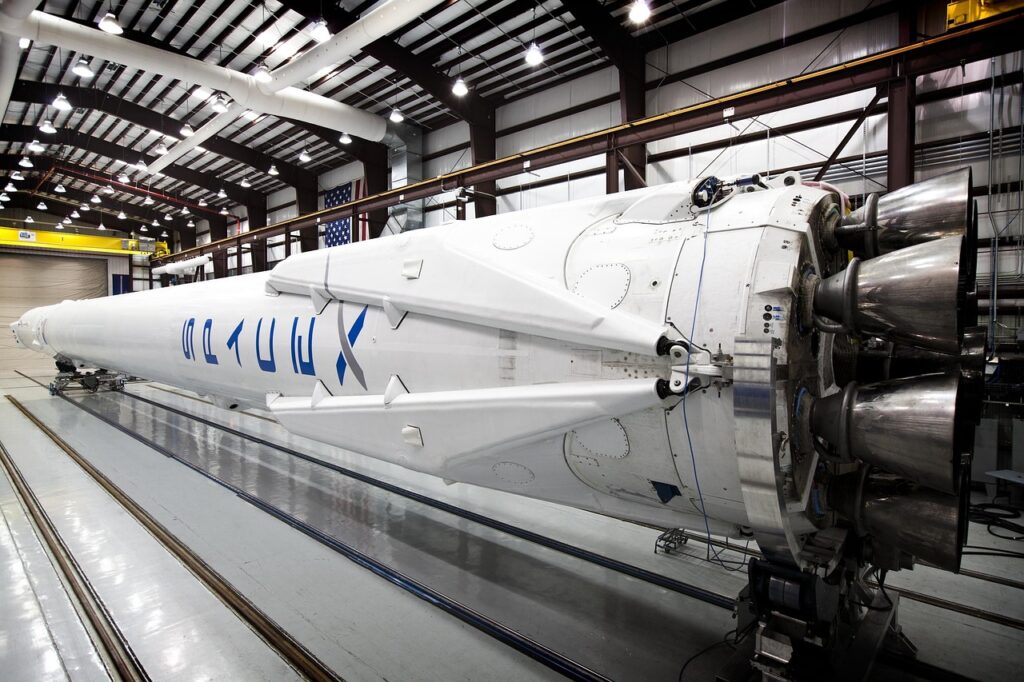 Das Bild zeigt eine Fabrikhalle mit Elektroautofertigung direkt neben einem Raketenstartturm, passend zur möglichen Elon-Musk-Fusion von Tesla und SpaceX – Foto: SpaceX-Imagery / Pixabay