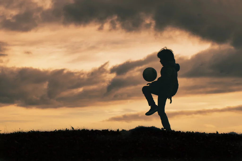Kleines Kind drippelt mit einem Fußball bei Abendstimmung