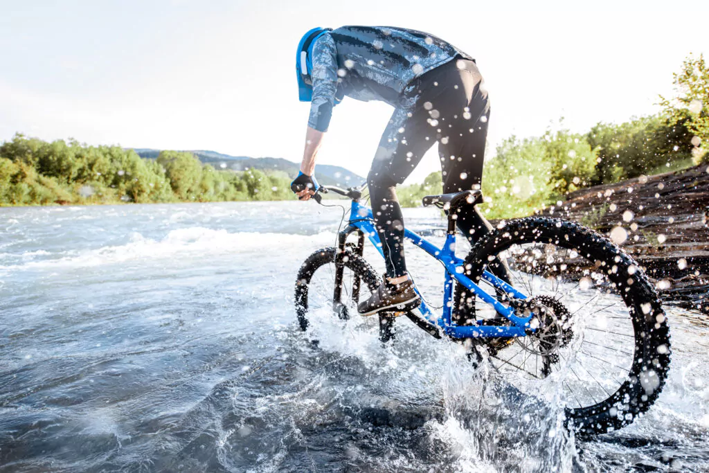 Mountainbiker fährt stehend auf dem Rad in einen Fluss