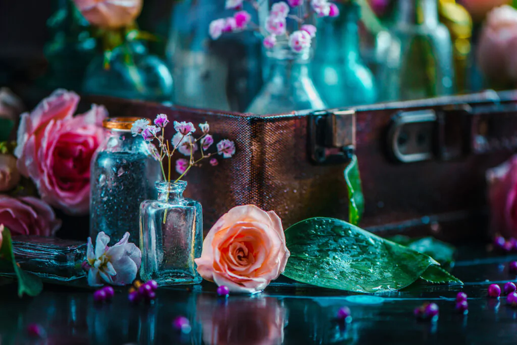 Viele Blumen in kleinen Vasen und Rosen die auf einem Glastisch liegen. Teilweise ist ein alter Koffer zu sehen