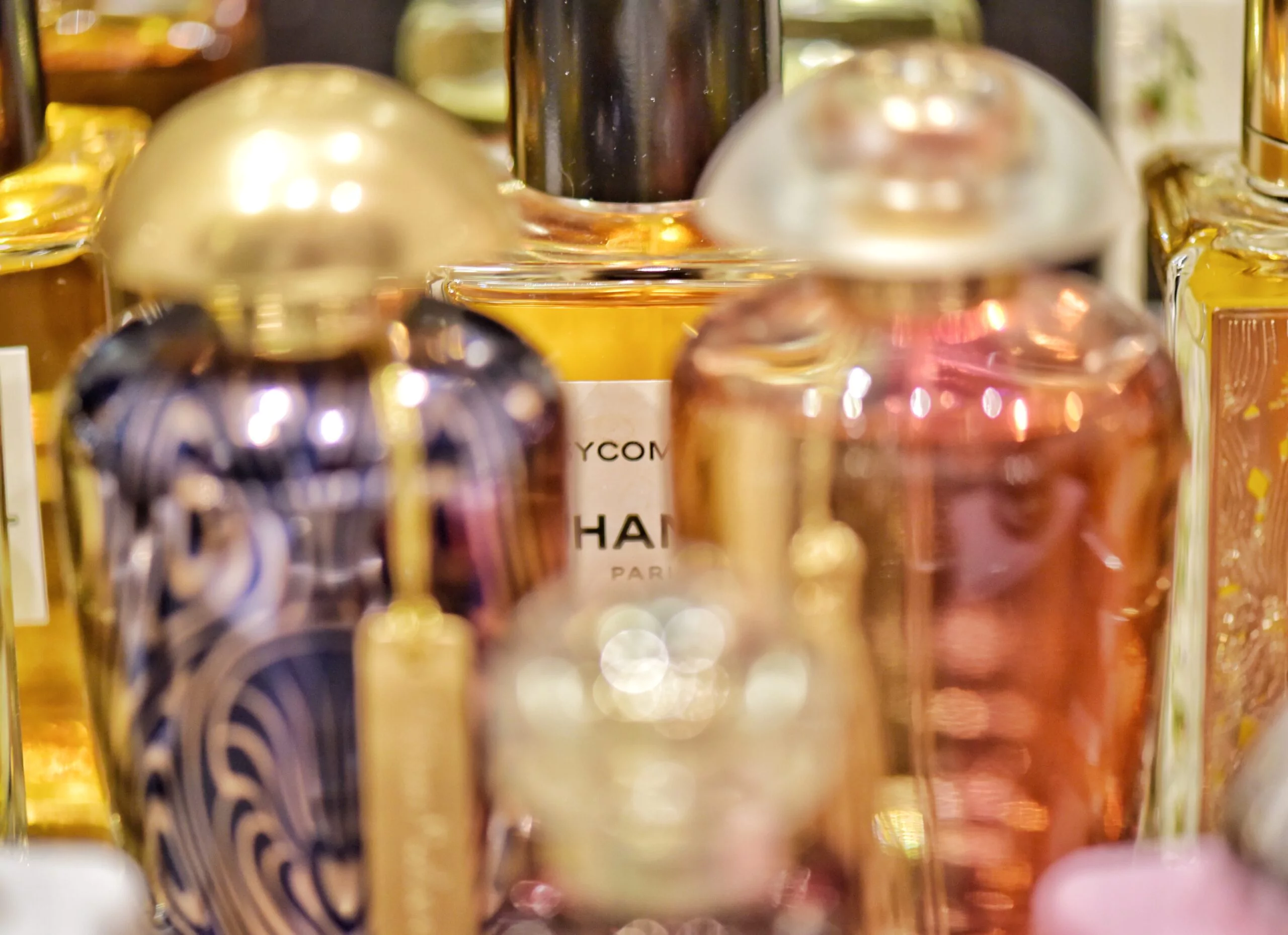 Parfumfalcones in dunkelviolett mit goldenem Verschluss sowie in rosarot mit gläsernem Verschluss. Dahinter ist ein Flacone von Chanel erkennbar